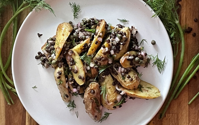 overhead view of fingerling and lentil salad on a plate beside a large serving bowl. Dill, shallot and dressing is scatter around.